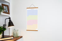 A vertical Spring wall calendar in Slate, hanging on a white wall in a bright room.